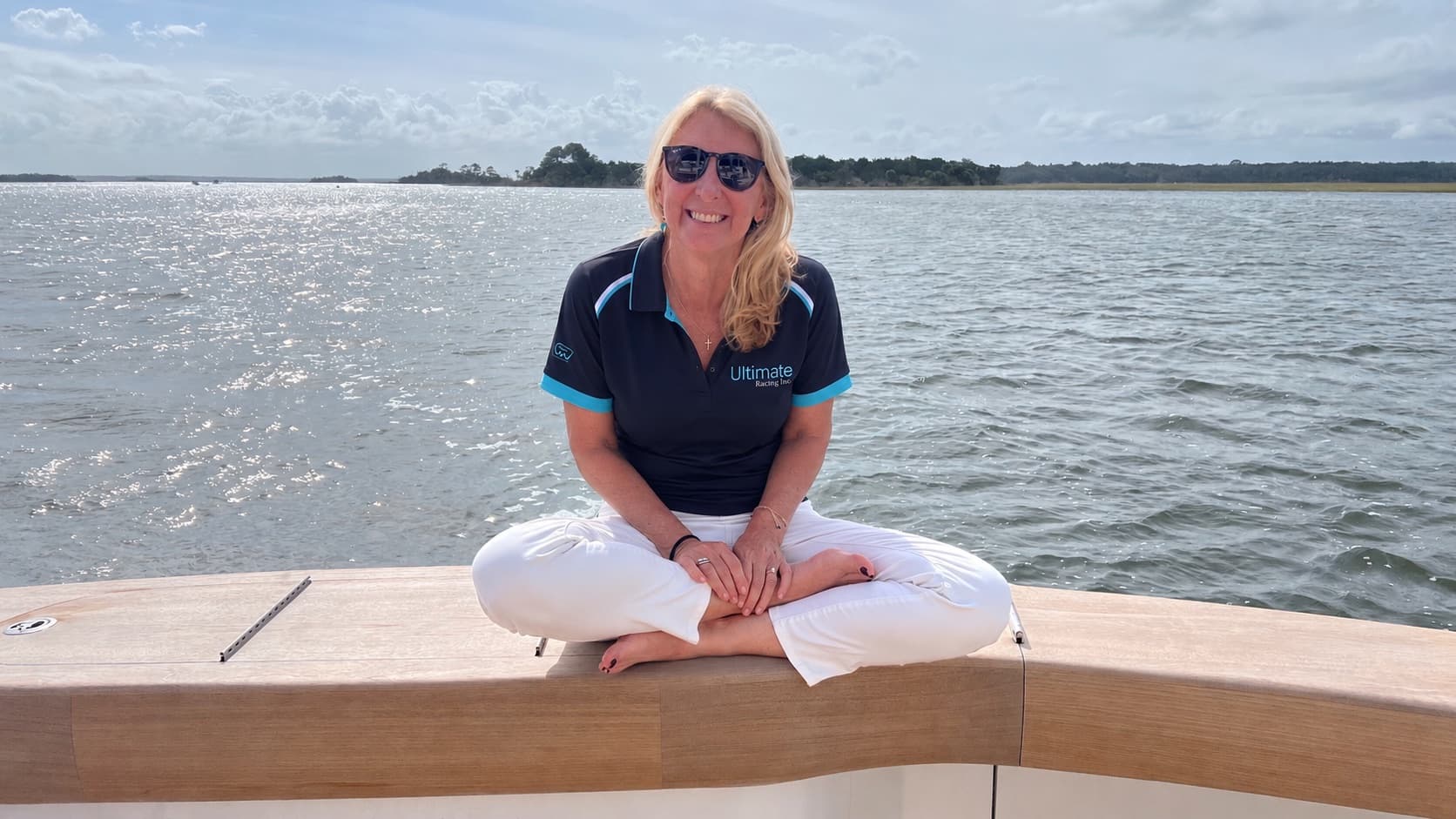 Angi Palmieri smiling in an Ultimate Racing polo, seated on a boat on the water.