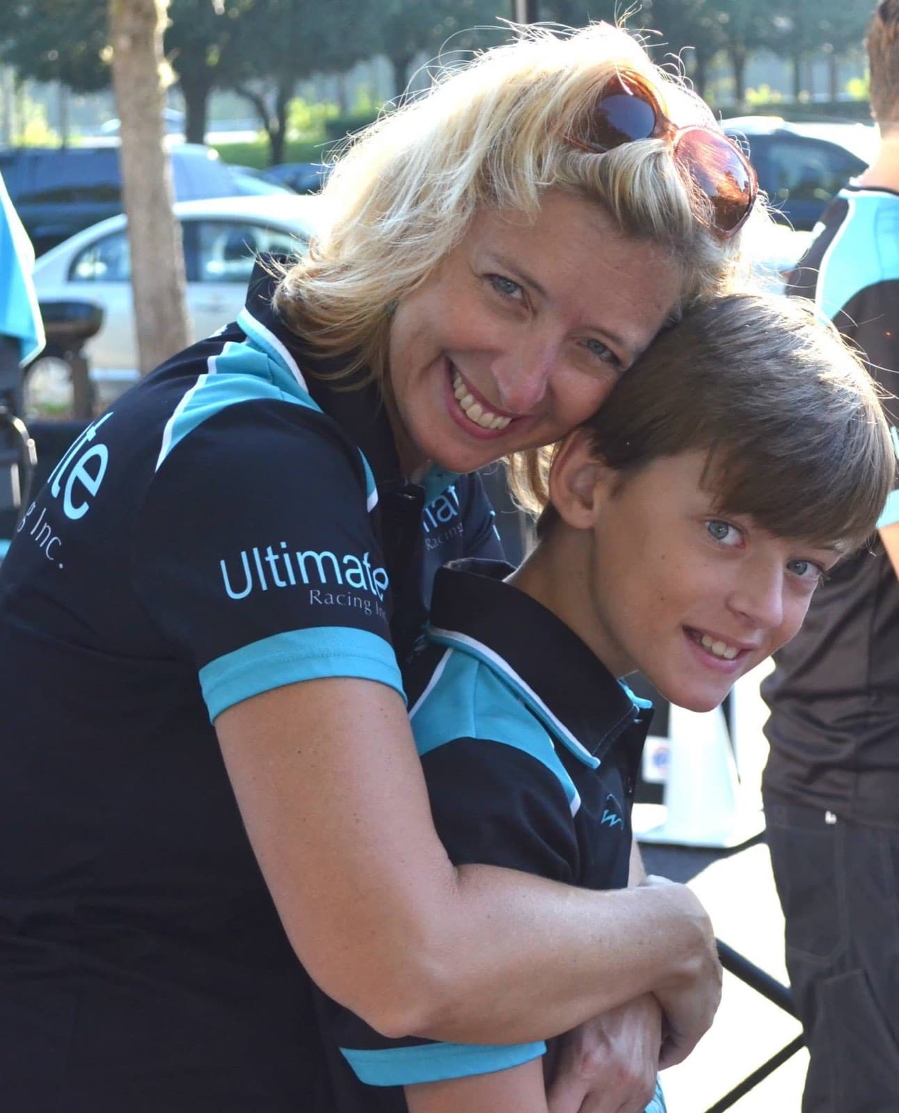 Angi Palmieri hugging a young Frank Palmieri cheek to cheek at an outdoor Ultimate Racing event, both in team polos.