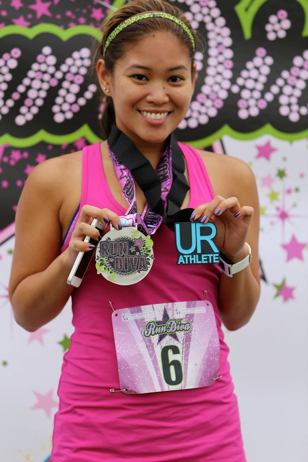 A runner smiling and holding up a finisher medal and event tag after a race